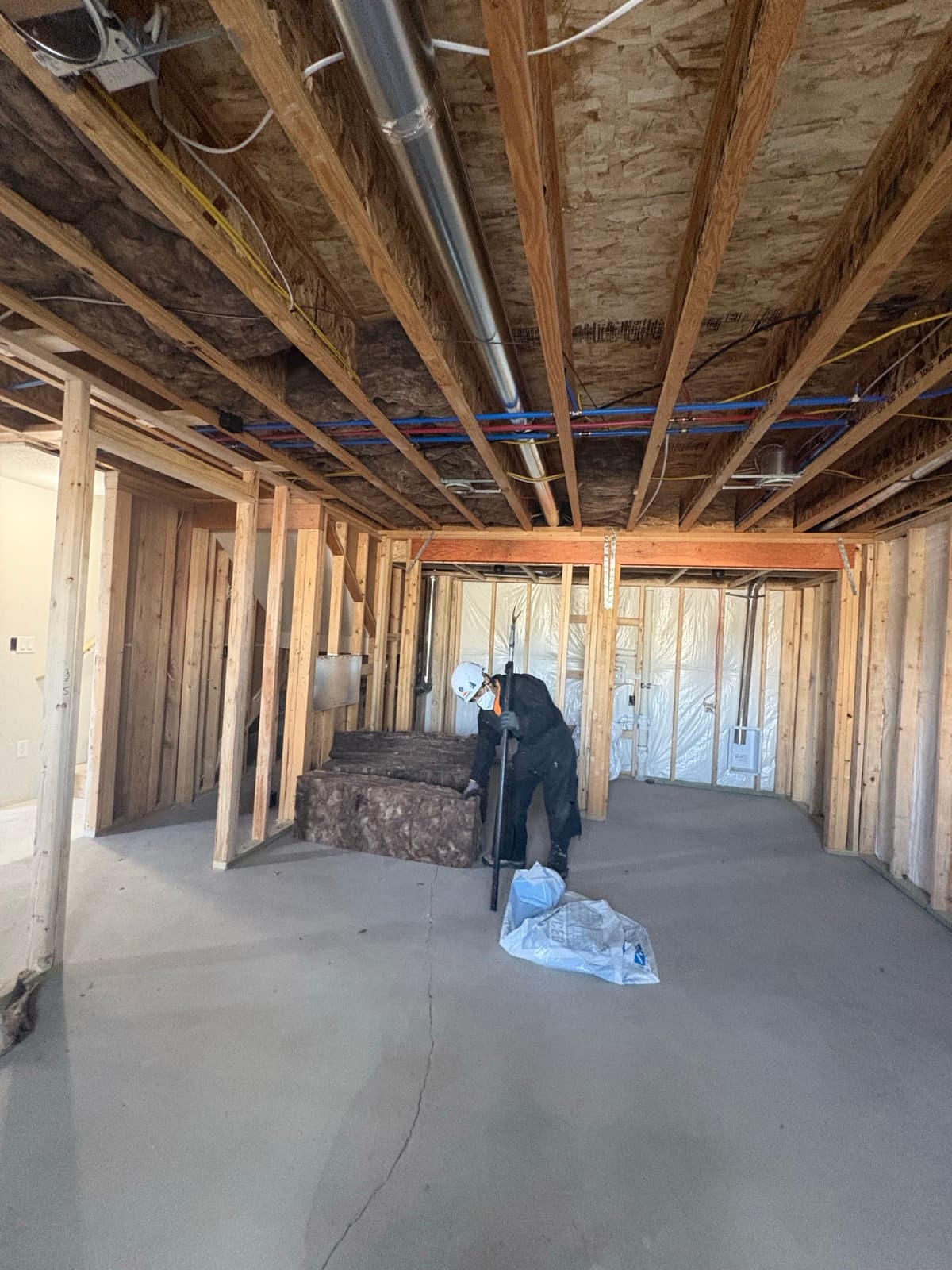 Crew member in protective gear staging insulation in a framed basement