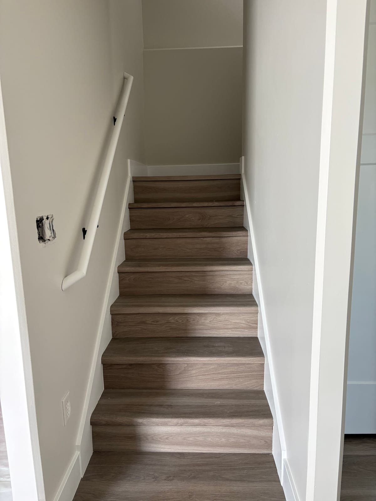 Finished basement stairs with white trim, painted walls, and a new handrail